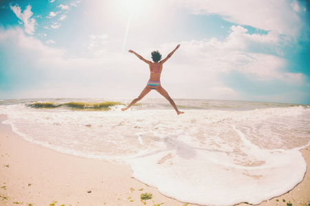 一个女孩在海滩上跳跃, 双手放得很宽。一个苗条的女人在海边休息。在海边的黑发。自然健身
