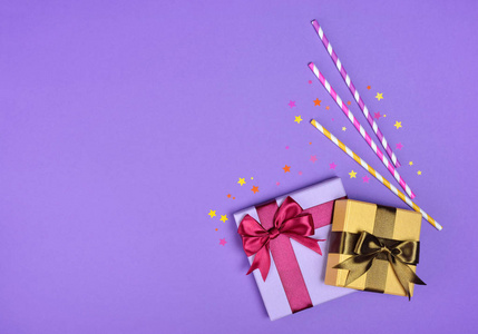彩色闪亮的经典礼品盒与缎弓和纸条纹鸡尾酒秸秆与五彩纸屑作为党的属性在紫色背景