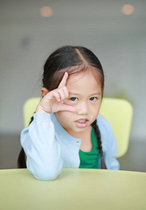 可爱的小亚洲儿童女孩躺在孩子们的桌子上看着相机