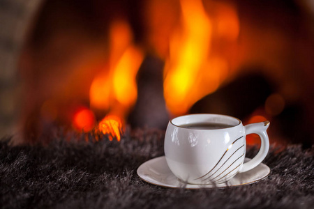 桌上壁炉旁边的白杯茶或咖啡。冬圣诞假期概念