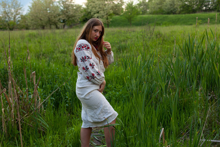 乌克兰女孩在亚麻长衬衫与刺绣诱人摆在一个绿色的春天草甸