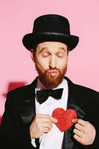 亲吻男人在燕尾服和顶帽子捧着一颗红色的心