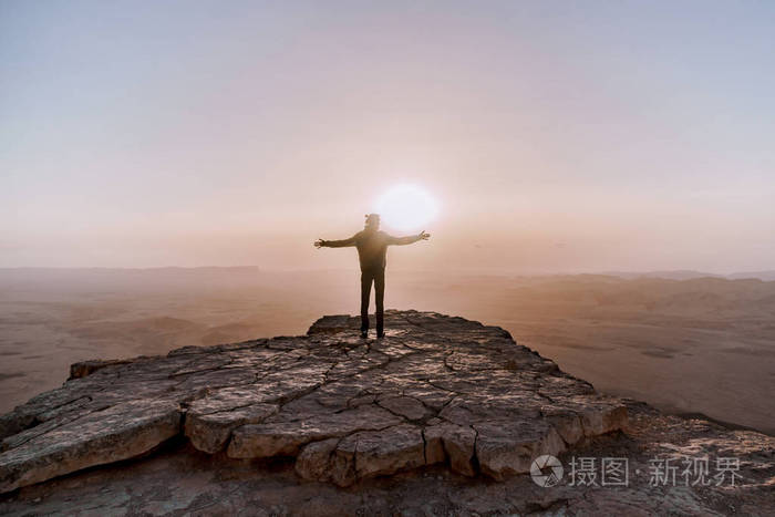 孤独的人在以色列南沙漠钦佩日出的看法.年轻男子站在悬崖边上