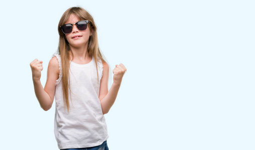 年轻的金发小孩戴着太阳镜尖叫着自豪和庆祝胜利和成功非常兴奋, 欢呼