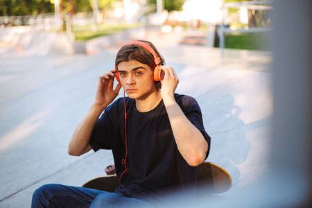 年轻的家伙在橙色耳机若有所思地看着相机听音乐与滑板在 skatepark