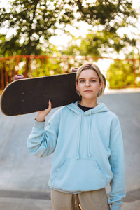 美丽的女孩在帽衫持有滑板在肩膀朦胧地看着在 skatepark 相机