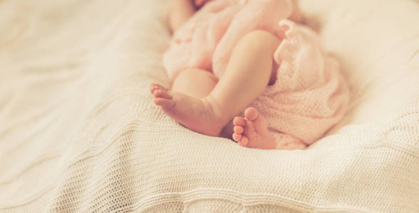 婴儿的腿裹在粉红色的毯子上, 躺在白色的针织毯子。选择性聚焦
