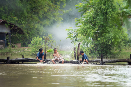 一群农村儿童坐在一起玩水在沼泽的木桥上, 在沙功的烟雾背景下, 泰国