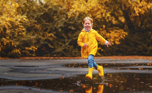 快乐的孩子女孩用伞和橡胶靴在秋天的沃尔玛的水坑里