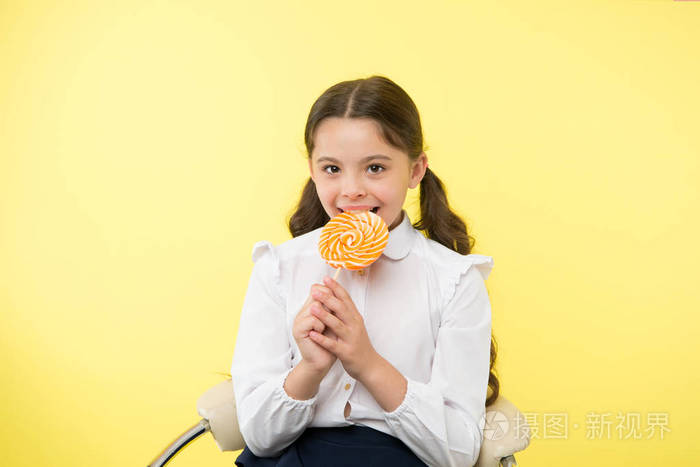 在黄色演播室吃棒糖的孩子.糖果吃糖与快乐的脸.孩子舔甜棒糖糖.