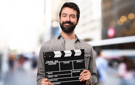 英俊的人与胡子举行 clapperboard 在室外