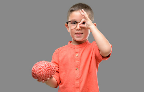 通过眼镜看戴眼镜的黑发小孩带着快乐的脸微笑着做 ok 标志用手在眼睛