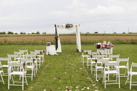 美丽的婚礼在一个白色的椅子领域。举行婚礼仪式, 婚礼拱门装饰用布, 鲜花和白色椅子两侧的拱门户外
