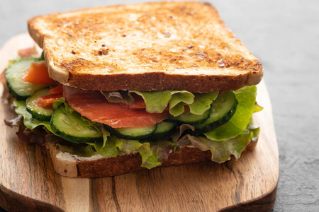 三明治配白面包敬酒, 红鱼鲑鱼, 新鲜绿叶沙拉和切片黄瓜在木板上