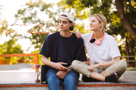 年轻的家伙与手机和漂亮的女孩与耳机高兴地看着一边花时间在 skatepark