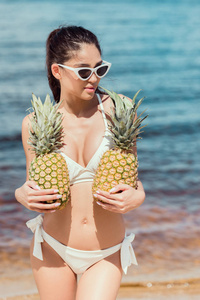 迷人的女孩在比基尼和太阳镜持有新鲜的菠萝附近的海