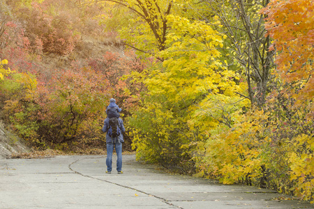 父亲和儿子在他们肩上步行穿过秋天的公园。后视图