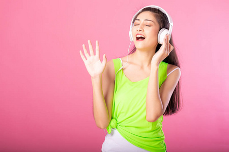 一个快乐迷人的女人的肖像在夏天的衣服听和跳舞的音乐与她的耳机隔离在粉红色背景