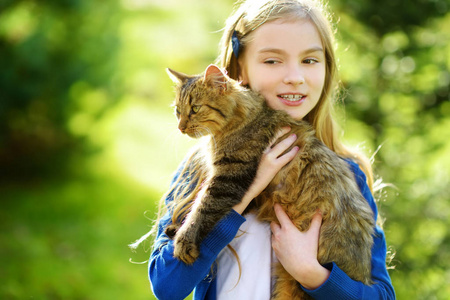 可爱的小女孩与她的猫在阳光明媚的秋天天。可爱的孩子抱着宠物小猫。儿童和动物