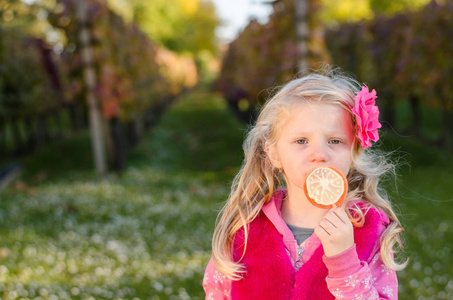 可爱的小金发女孩在秋天葡萄园与棒糖糖果
