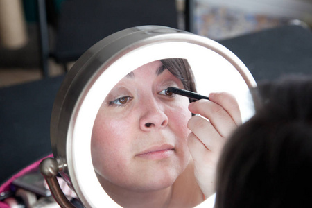 在镜子里, 一个女人小心翼翼地将黑色衬垫应用到她的眼皮上。