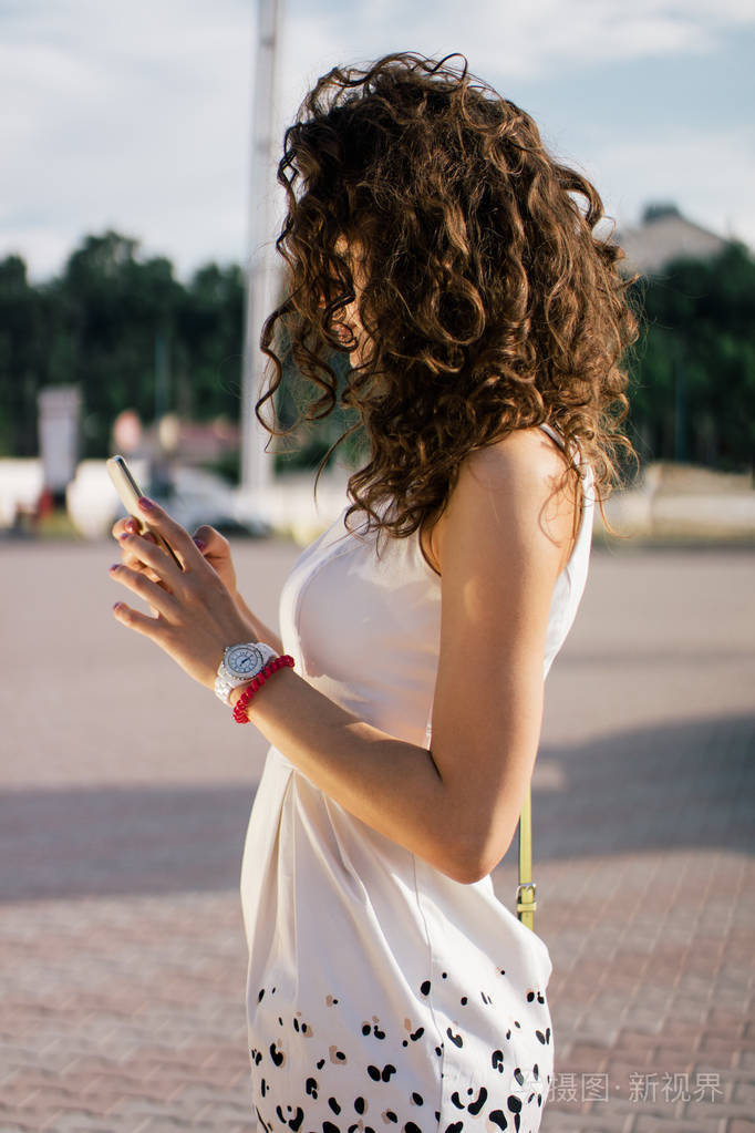 侧面观看年轻女子穿着白色礼服使用她的智能手机.