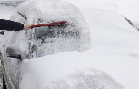 女孩用刷子把车从雪地上刷下来。