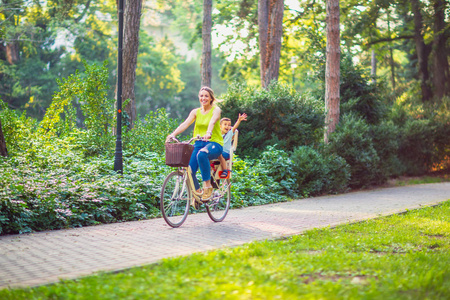 幸福的家庭。微笑的母亲和儿子骑自行车在城市公园。家庭体育与健康生活方式