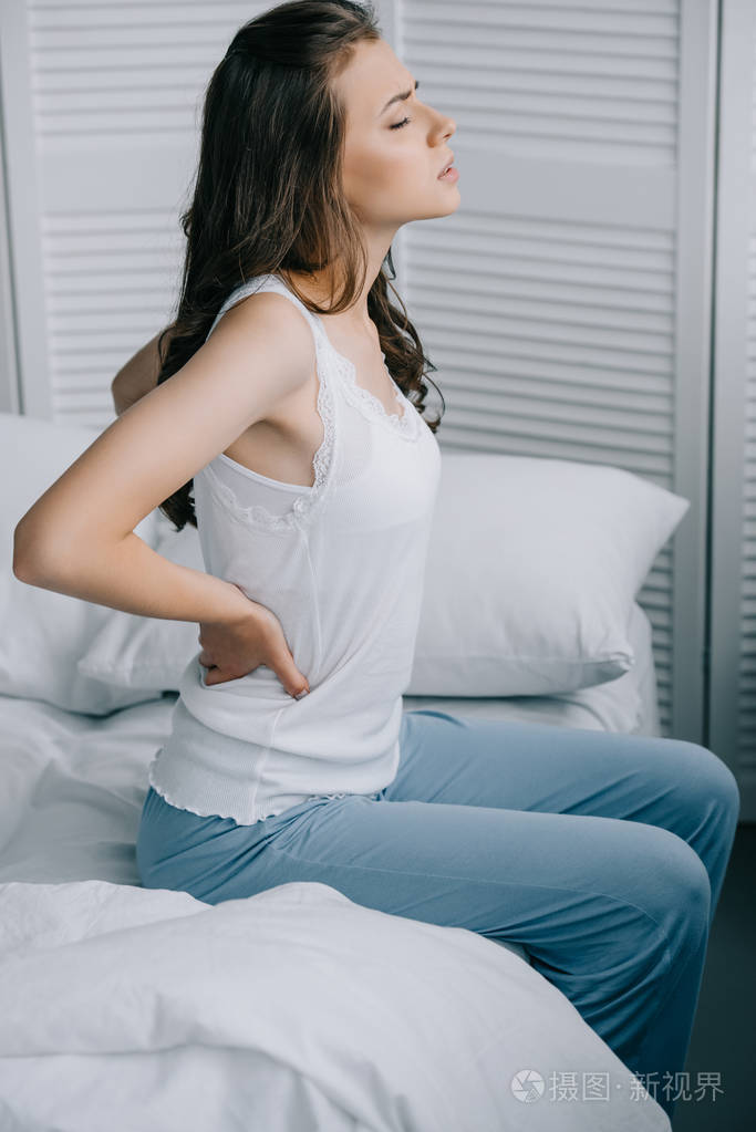 从床上背痛看穿着睡衣的年轻女子的侧面照片-正版商用图片0usdsb-摄图