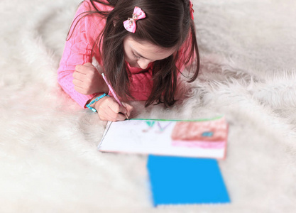 小女孩用铅笔画画, 躺在起居室的地板上。