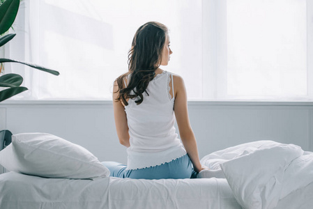 背部穴位图坐在床上看着的穿着睡衣的年轻女子的背部视图照片