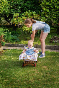 孩子坐在一辆木制推车里, 他的姐姐在夏日花园里翻滚着。