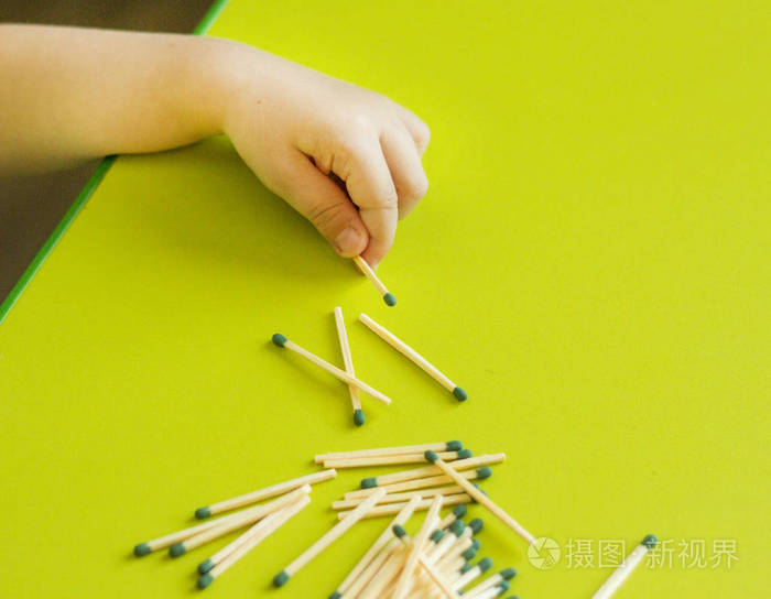 一个小孩子在绿色背景,特写,危险,火灾,孩子和火柴的手上握着一根火柴