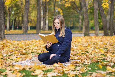 年轻的怀孕女孩读了一本书, 坐在一个秋季公园的格子。秋季和户外休闲的概念
