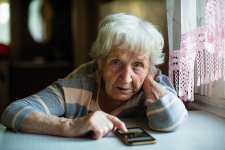 一个坐在桌子旁的智能手机的老年妇女