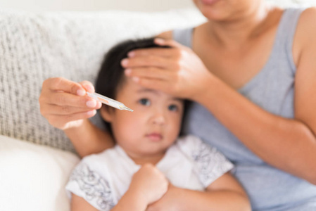 母亲在家里的起居室的沙发上用温度计来检查她生病婴儿的体温。医疗保健理念