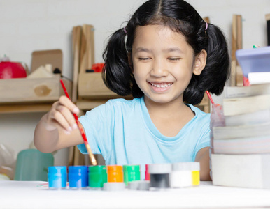 亚洲小女孩正用微笑和滑稽的色彩在桌子上玩, 用红色的刷子蘸上了颜色。选择 焦点浅景深 字段