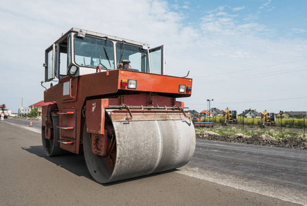 在沥青路面工程中进行道路修复的橙色重型振动压路机。在新的道路建设工地工作。修复