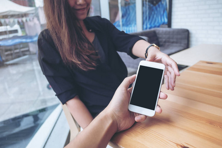 一个男人的手拿着白色的手机和空白的黑屏给咖啡馆的女人的样机图像