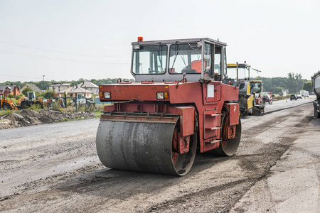 在沥青路面工程中进行道路修复的橙色重型振动压路机。在新的道路建设工地工作。修复