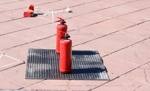 两个红色金属大手动二氧化碳或灭火器灭火站在黑色橡胶介质地毯上的地板上