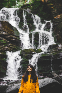 微笑的女人穿着黄色的雨衣, 背景是瀑布。徒步旅行概念