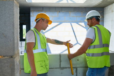 两个建筑工人的肖像穿 hardhats 和反光背心检查混凝土砌块墙体水平