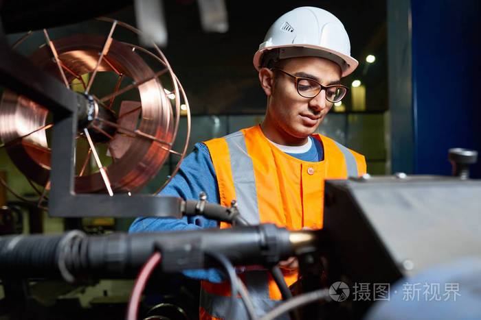 身穿防护头盔和眼镜的英俊年轻工人站在生产部的现代工厂和操作机器, 肖像拍摄