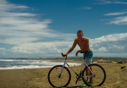 生活理念快乐的年轻有魅力的男子站在自行车沿夏季海滩