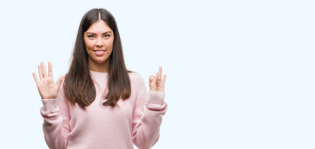年轻漂亮的西班牙裔妇女穿着毛衣显示和指向七的手指, 而微笑的信心和快乐