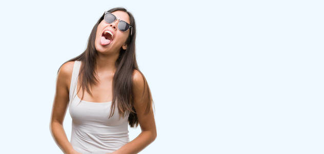 年轻漂亮的西班牙裔戴着太阳镜, 舌头露出快乐的表情。情感概念