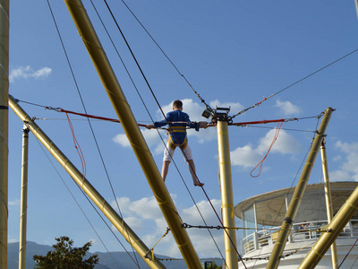 男孩高兴地跳上在游乐园的蹦极对蓝天照片
