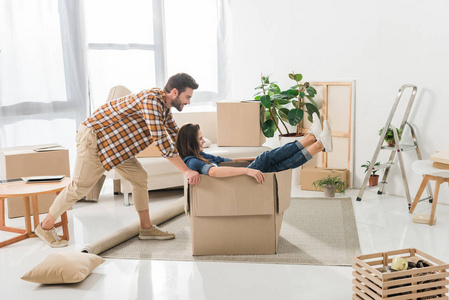 夫妇有乐趣与纸板盒在新房子, 搬家概念的侧面视图