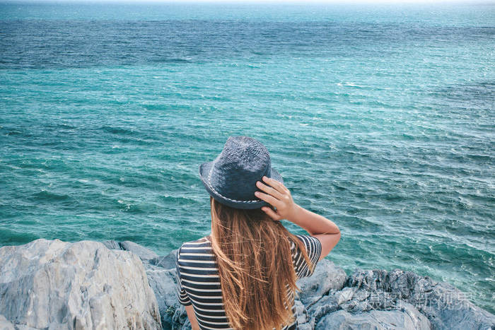 一个戴着帽子的女孩正享受着美丽的海景, 或坐在海边的大海.
